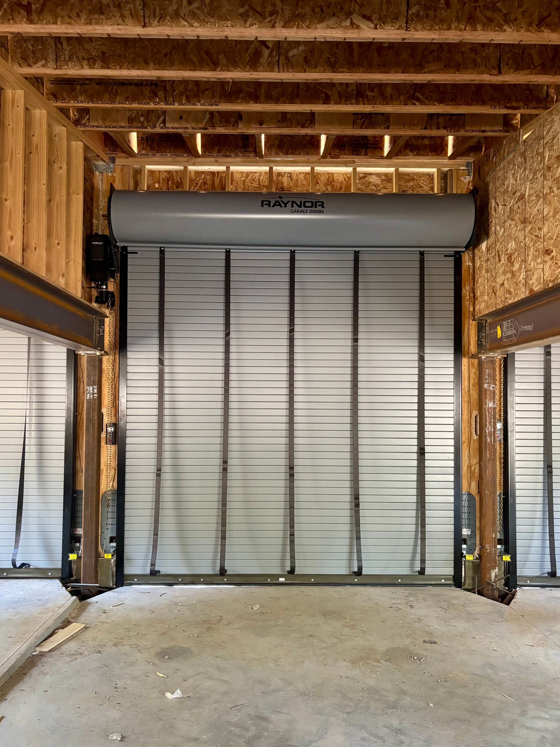 A gray industrial roll-up door installed between wood-framed walls in an unfinished construction space.