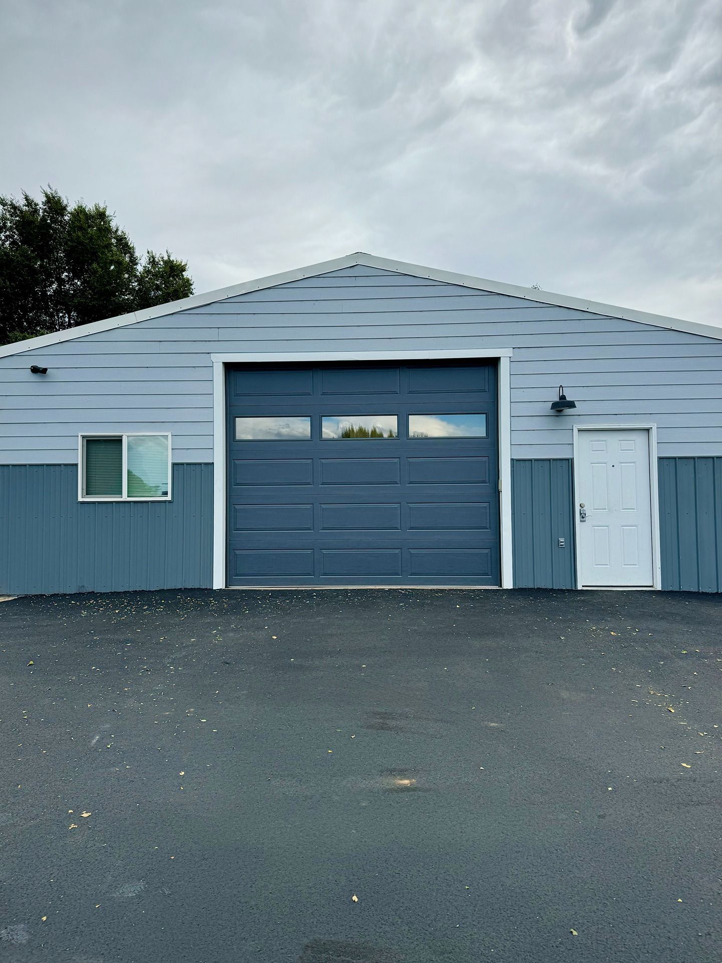 A single-story, light and dark blue metal building with a central garage door, a side entry door, and a single window.
