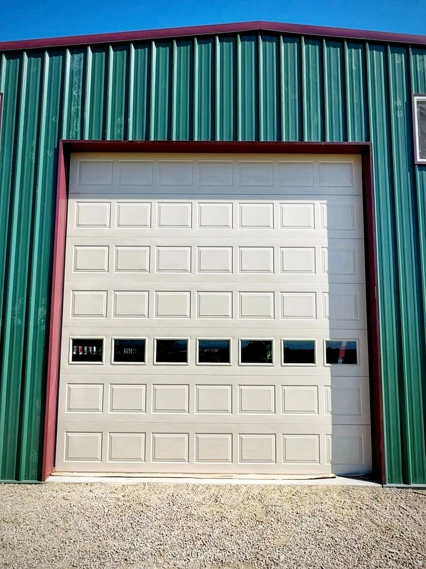 A white, multi-paneled garage door with a row of windows, set within a green metal building exterior.