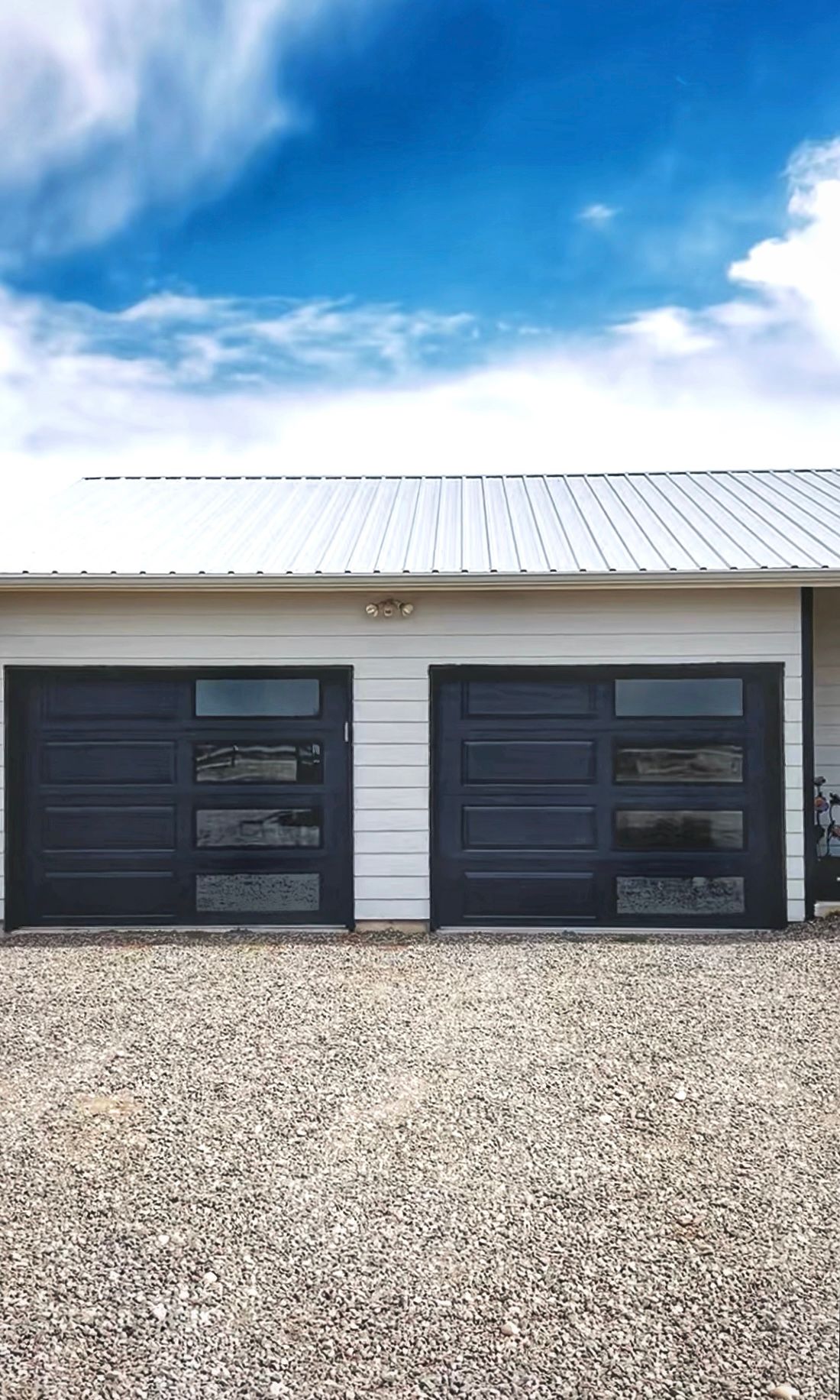 A white building with two modern dark grey garage doors featuring horizontal windows under a bright blue sky.