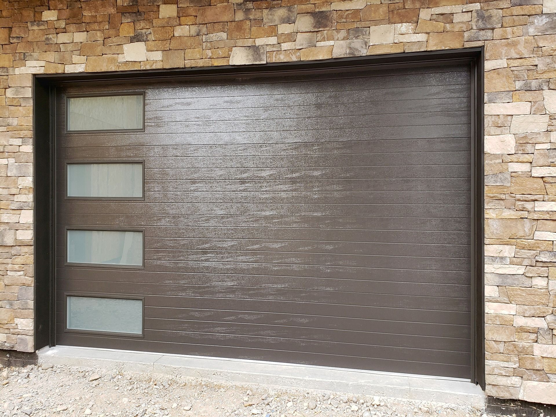 A dark brown, horizontal-slatted modern garage door with a vertical row of four frosted glass windows on one side.