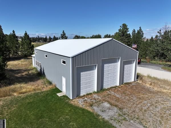 Gray metal garage with three white doors, seen from above in a rural setting