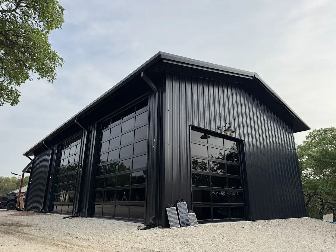 Black metal barn-style building with large garage doors on a gravel lot
