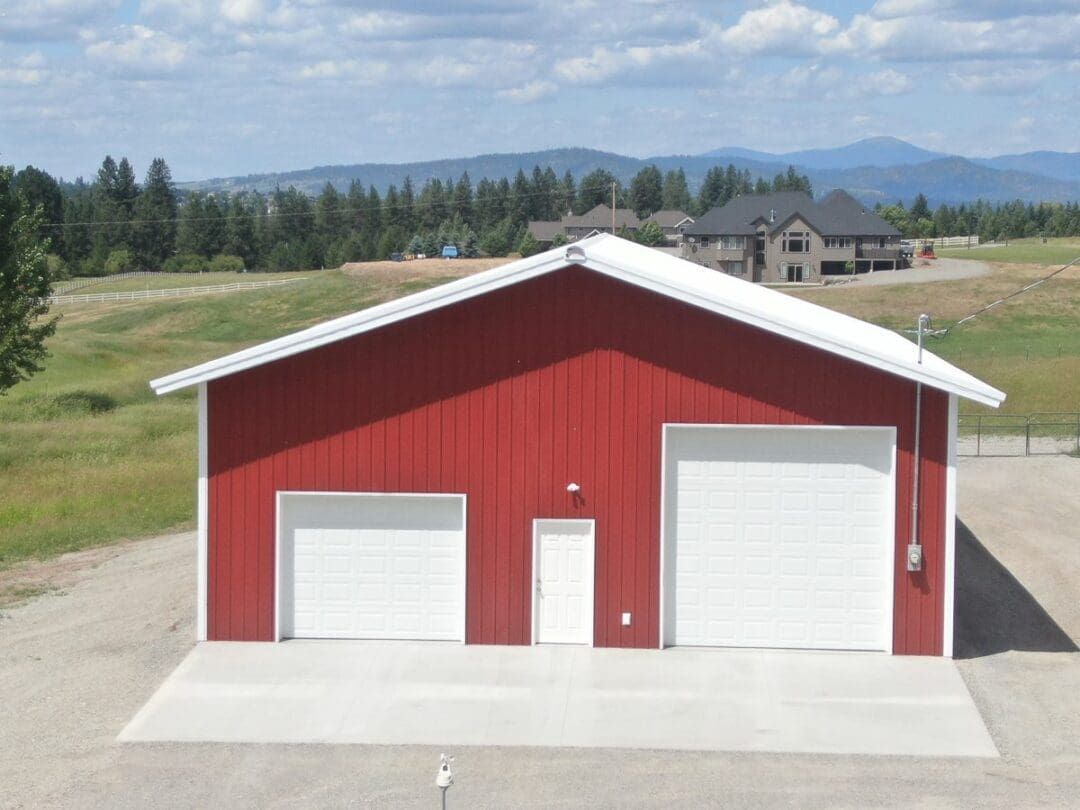 Red barn-style garage with three white doors in a rural field, with mountains in the background.