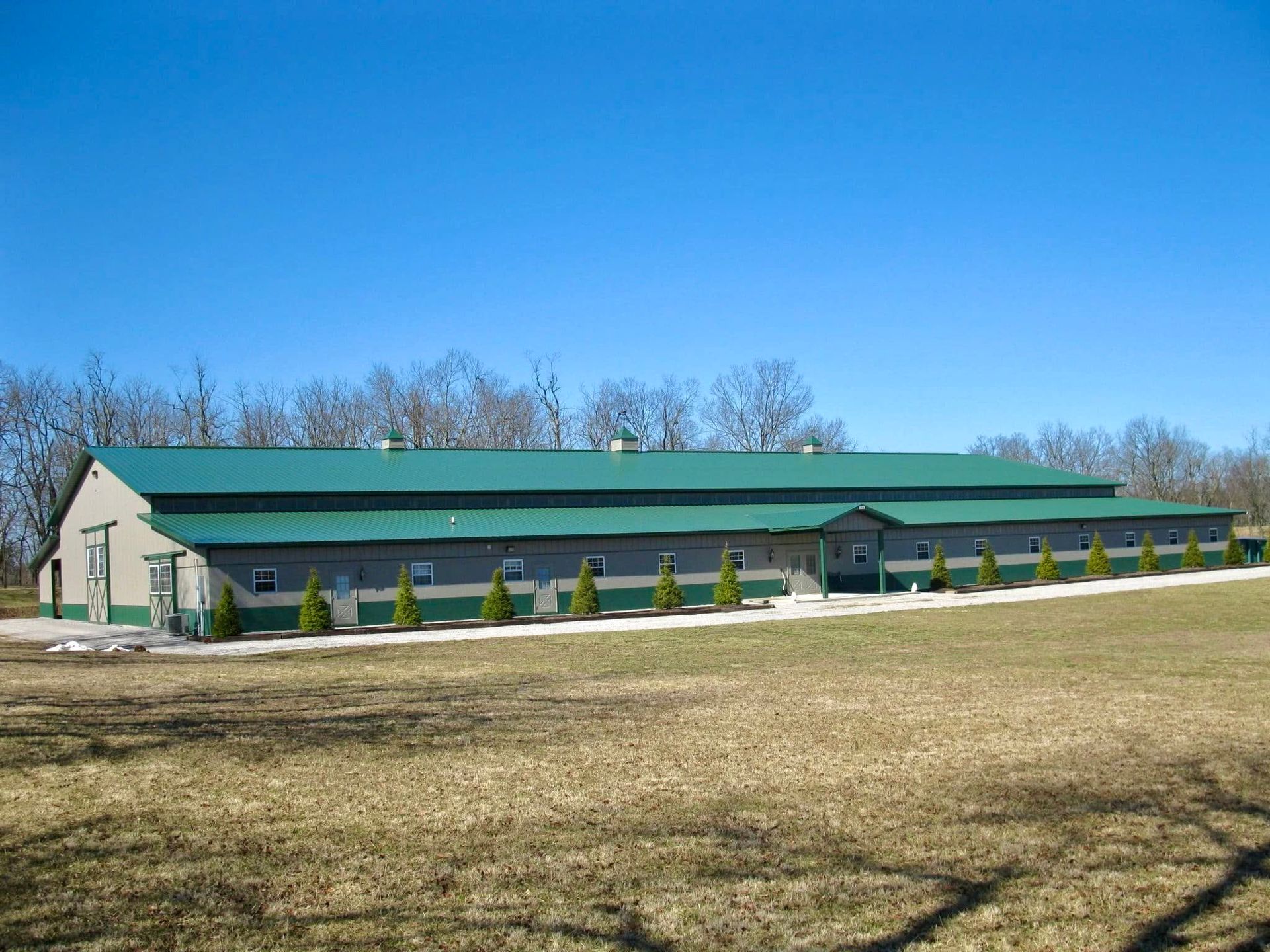 Long green barn-like building on a grassy field under a clear blue sky