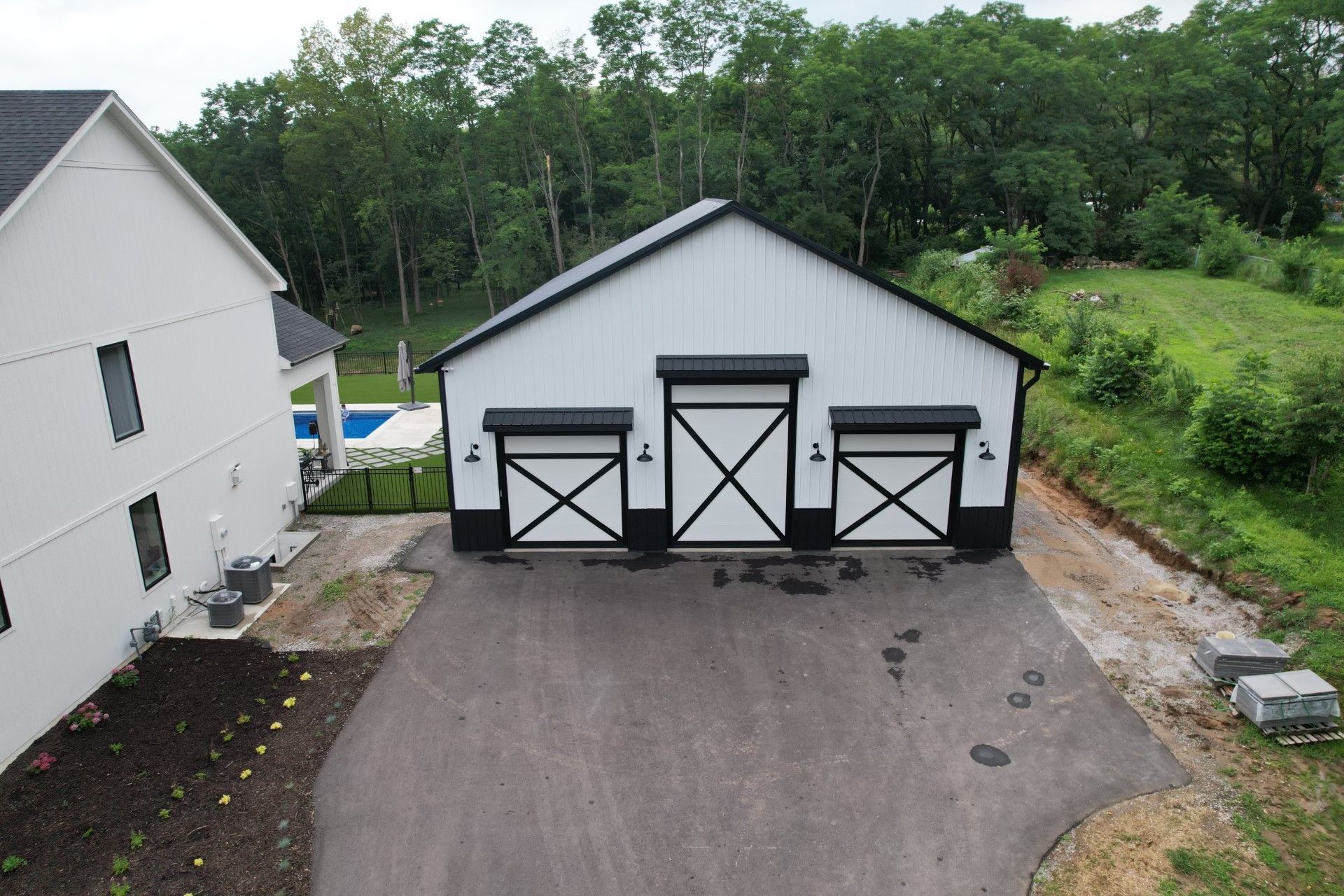 White three-bay garage with black trim beside a house, set on a paved driveway near trees.