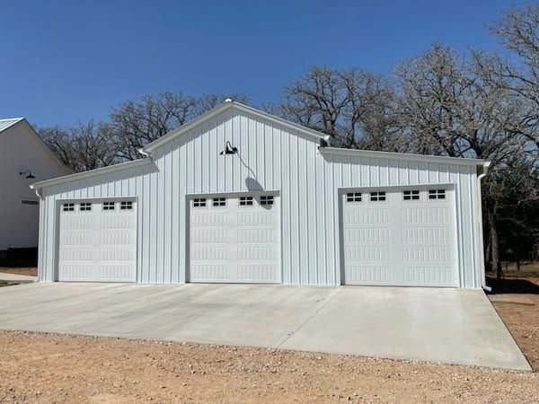 White metal three-bay garage with concrete driveway and trees in the background
