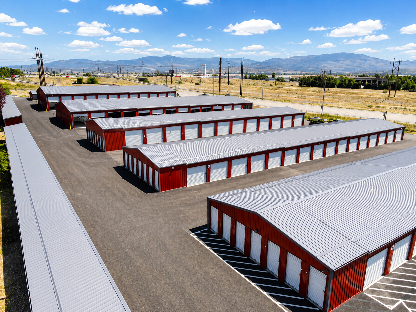 Aerial view of rows of red and white storage units in a fenced industrial lot under a blue sky.