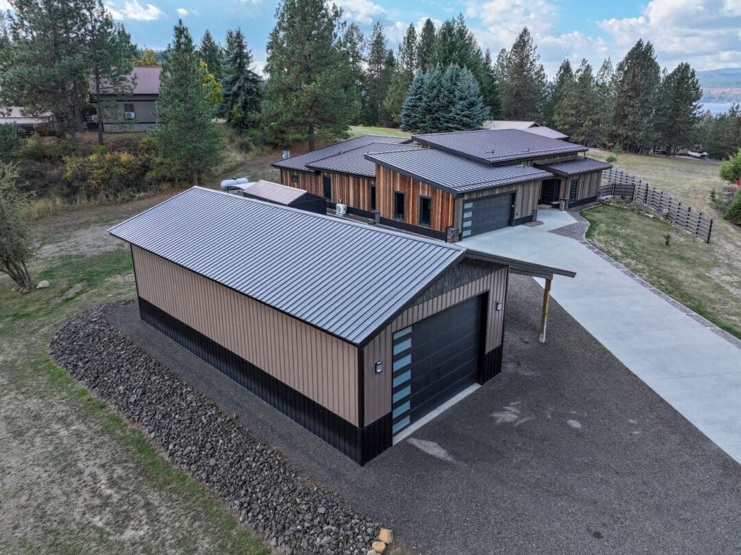 Modern house with metal roofs and wood siding, seen from above on a gravel driveway surrounded by trees