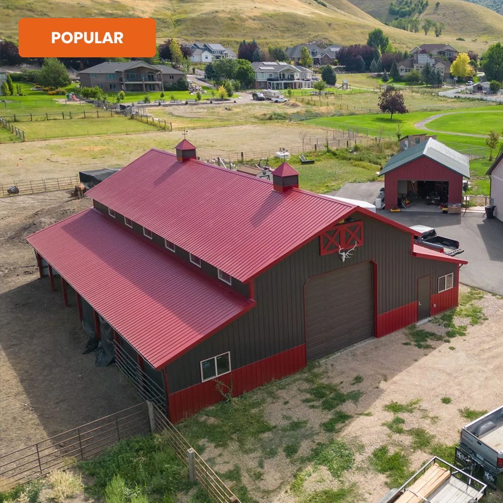 Aerial view of a red barn and outbuilding in a rural field with hills and houses nearby