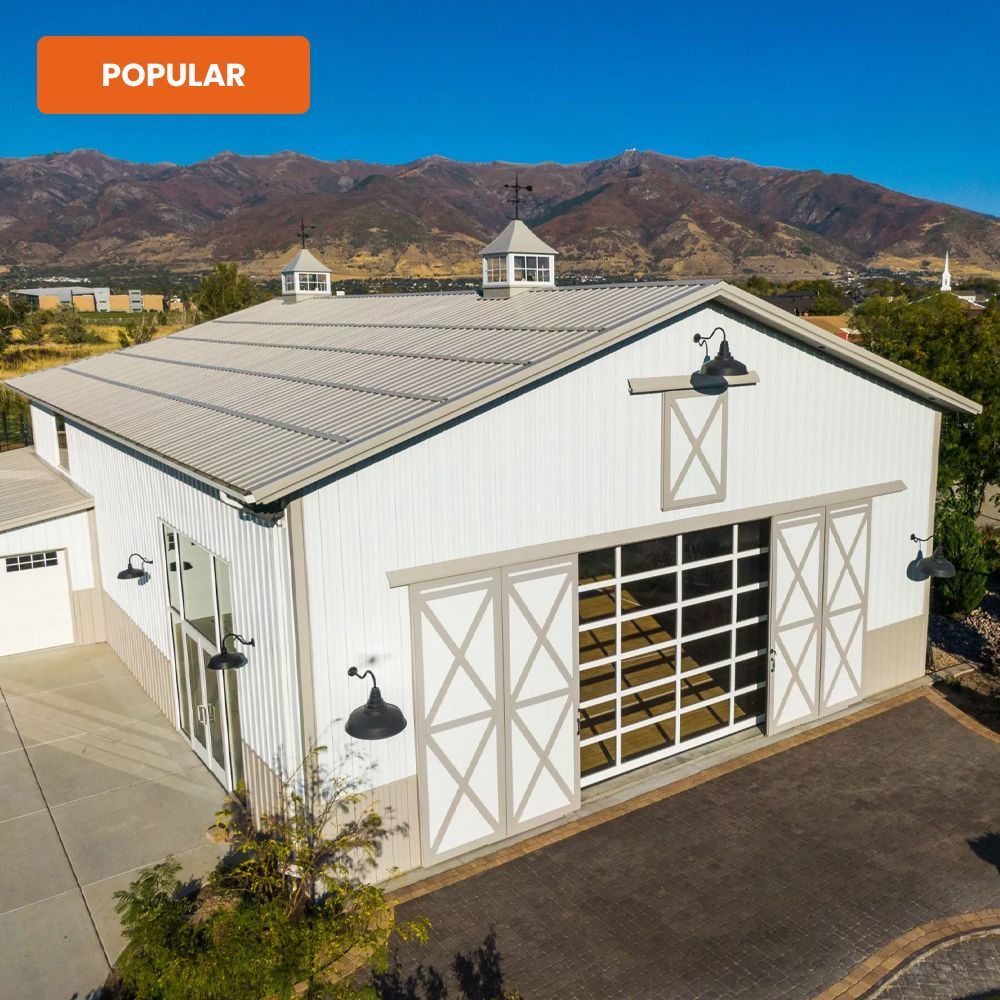 White barn-style building with large sliding doors, black trim, and mountains in the background