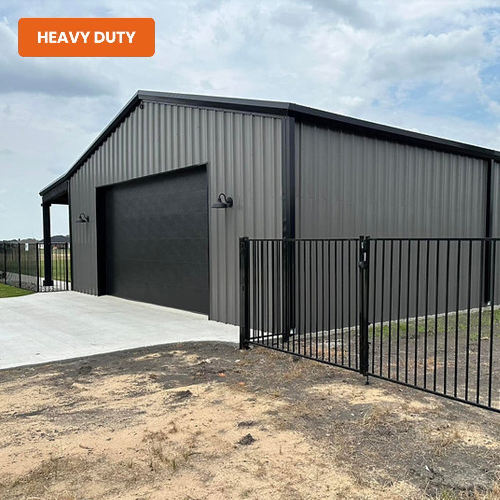 Gray heavy-duty metal garage with a black roll-up door and fenced driveway under a cloudy sky