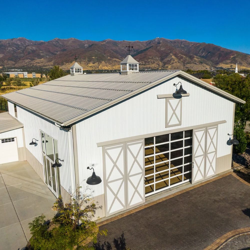 White barn-style garage with large open door, set against mountains under a clear blue sky.