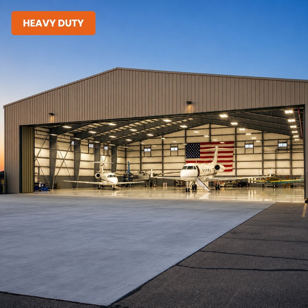 Large aircraft hangar with two small planes inside and a wide open hangar door at dusk