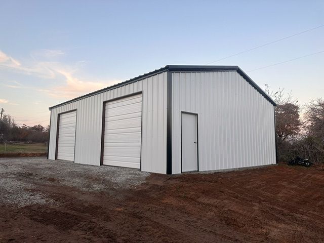 White metal storage building with two roll-up doors on a dirt lot at dusk