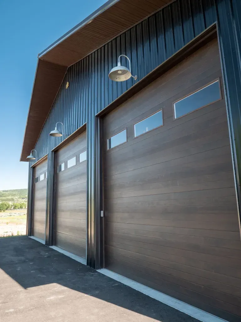 Modern brown industrial building exterior with large garage doors and wall-mounted lights