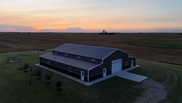 Modern barn-style house with gray siding at sunset in a rural field