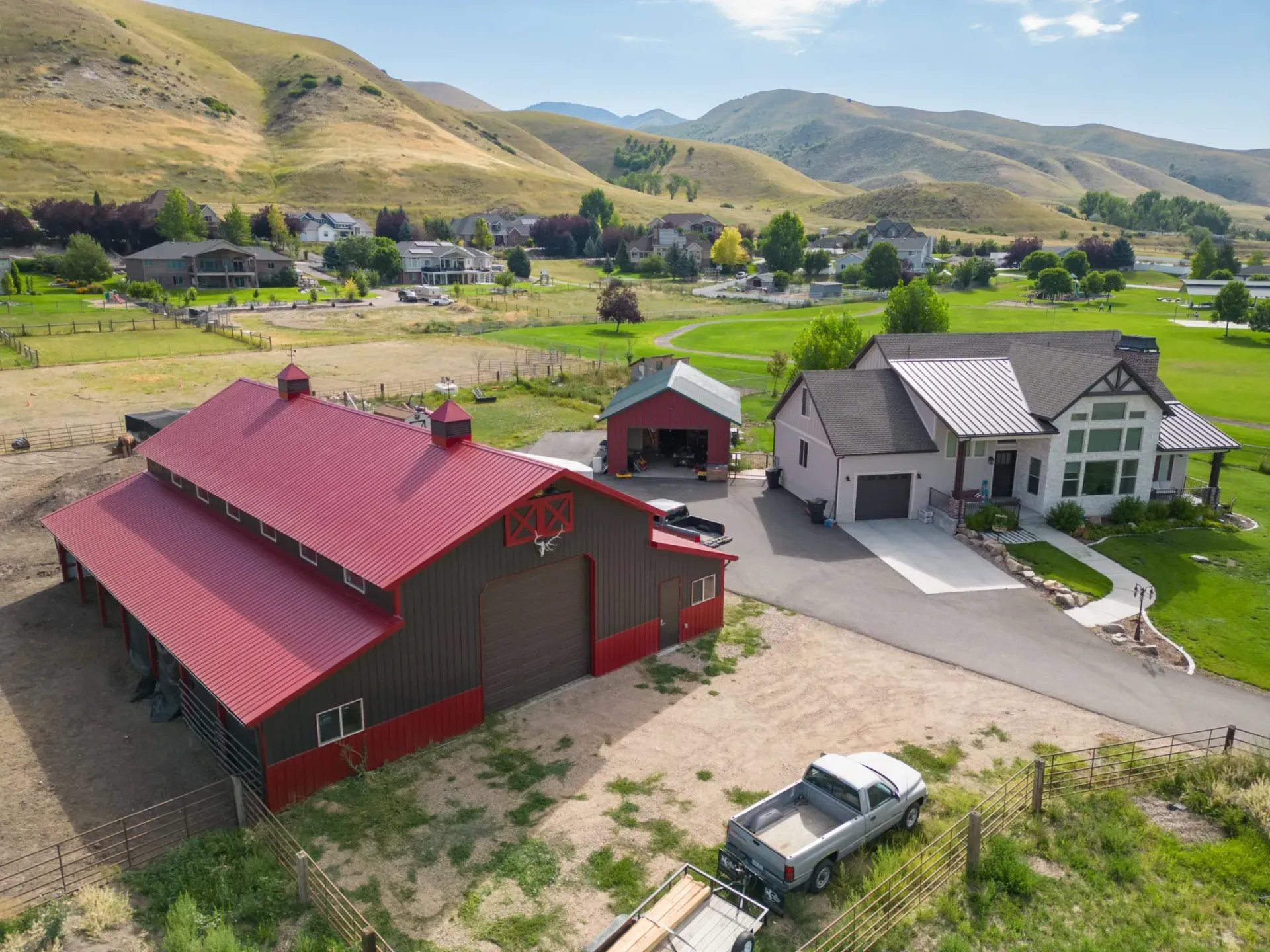 Aerial view of rural houses with red and gray roofs in a green valley, backed by hills and mountains.
