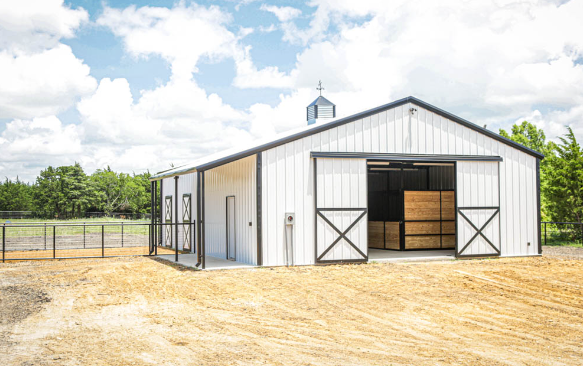 White metal barn with open double doors on a dirt lot under a cloudy sky
