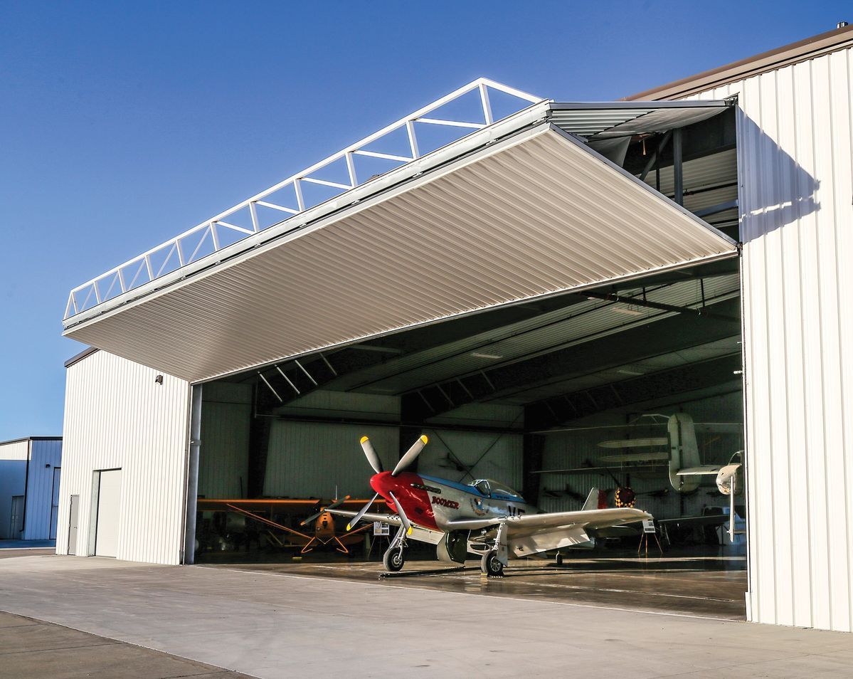 Small airplane parked in an open hangar with a large door raised in daylight