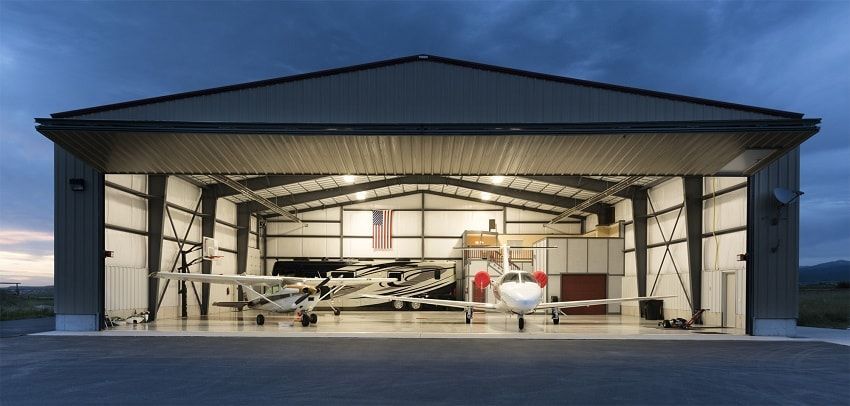 Open hangar with a small airplane and a person in red gear standing inside at dusk