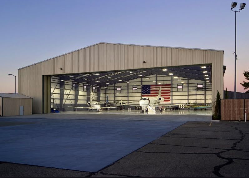 Large open hangar with a small airplane inside, lit at dusk with a U.S. flag on the back wall.