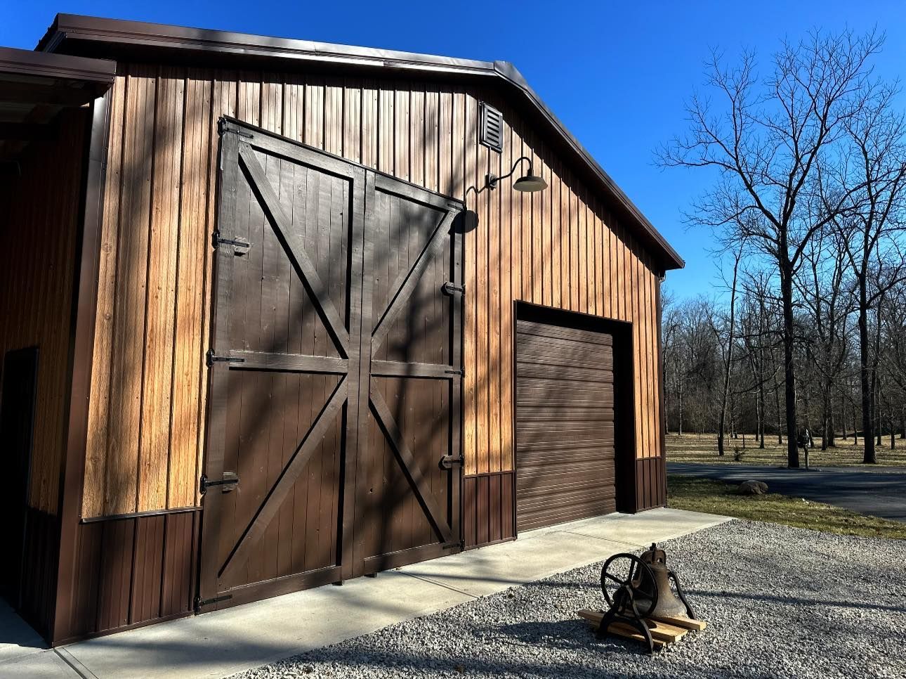 Rustic wooden barn with large doors beside a gravel path on a sunny day