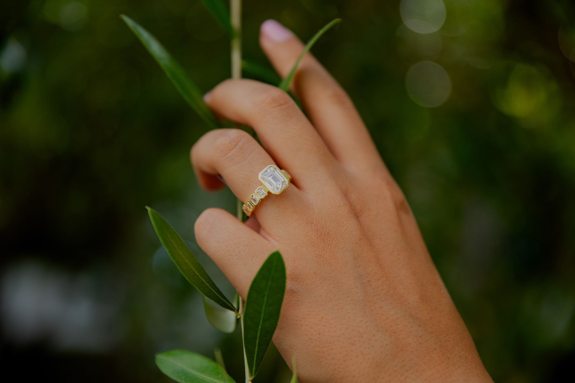 Hand with gold ring resting among green leaves against a blurred dark background