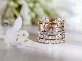 Stacked gold and diamond rings beside a white flower on a soft, blurred background