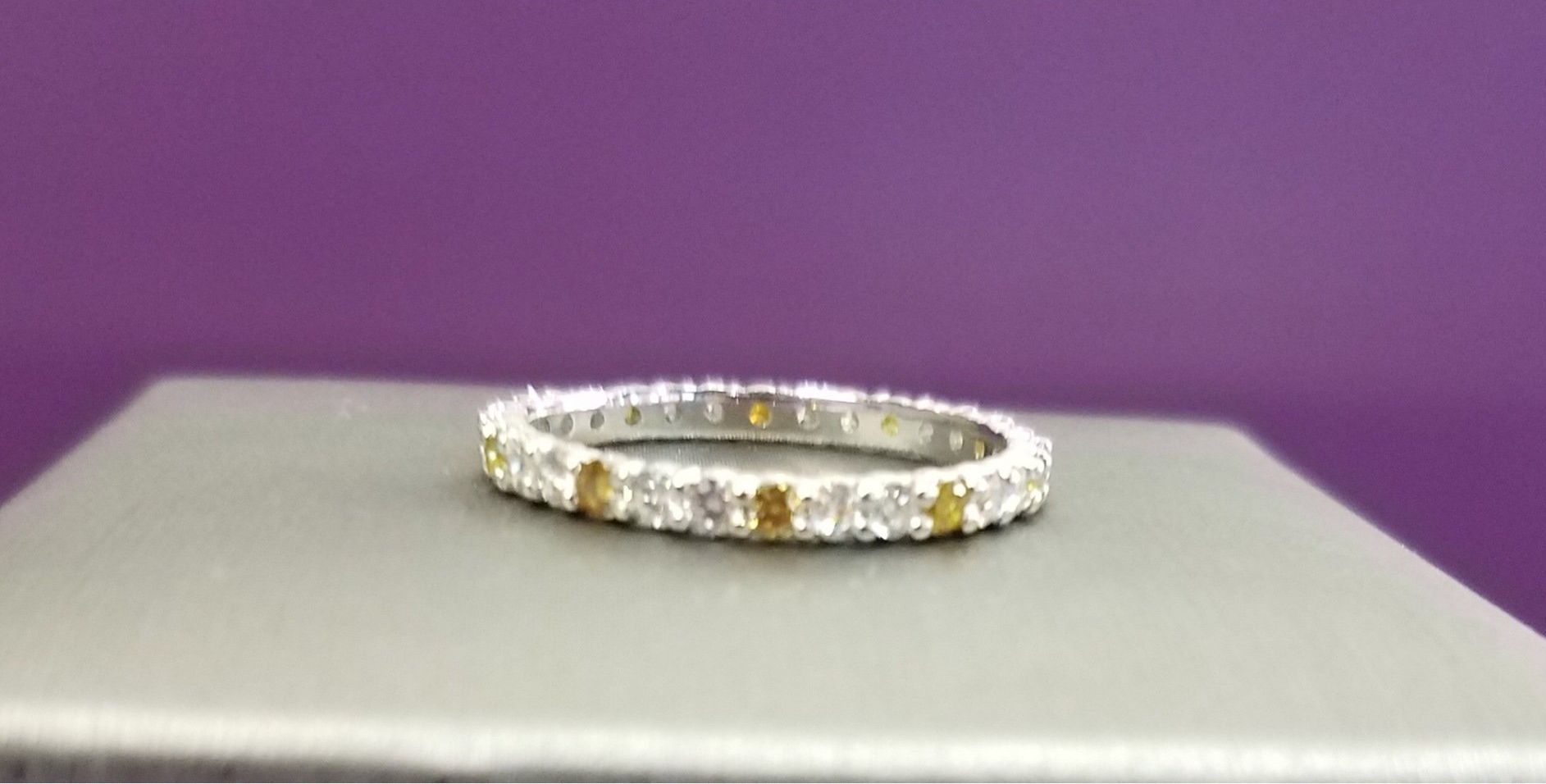 Silver and gold ring with clear stones on a gray display stand against a purple background