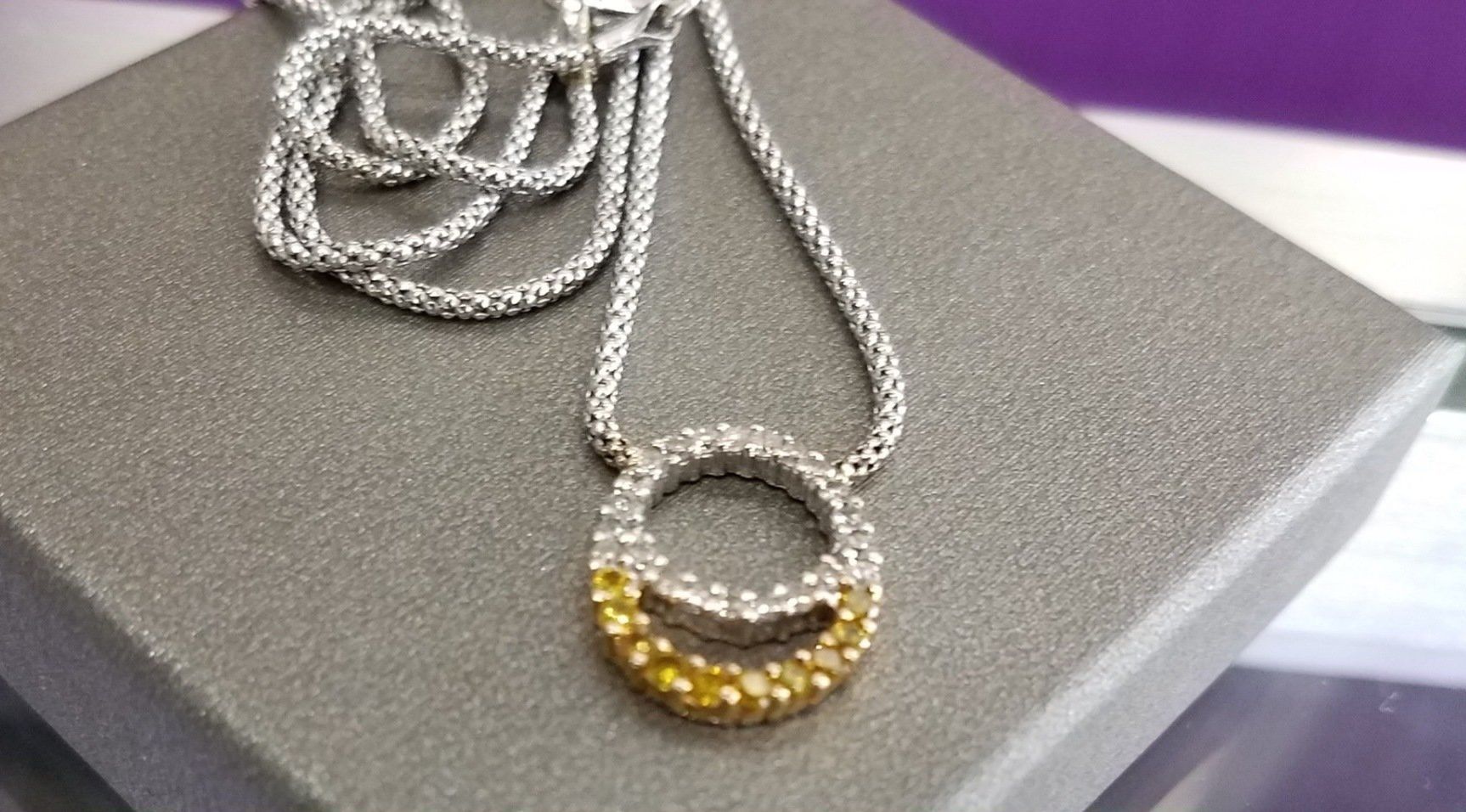 Silver necklace with a circular pendant accented by small gold beads, resting on a gray surface