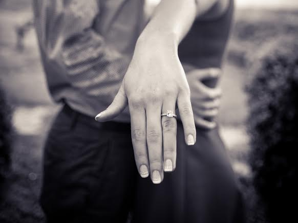 Close-up of two clasped hands, one showing a wedding ring, in black and white.