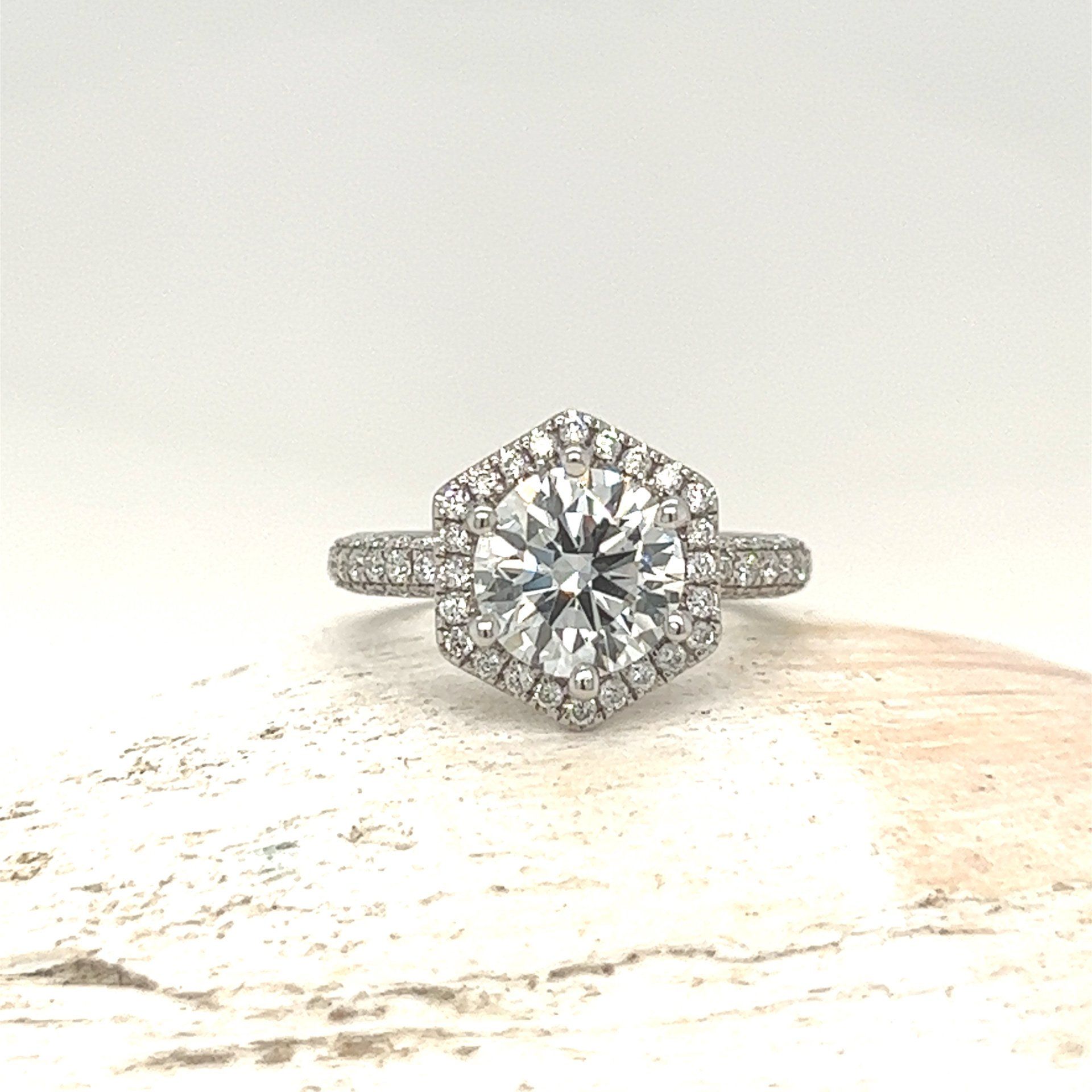Diamond halo engagement ring on a light textured surface, centered against a white background