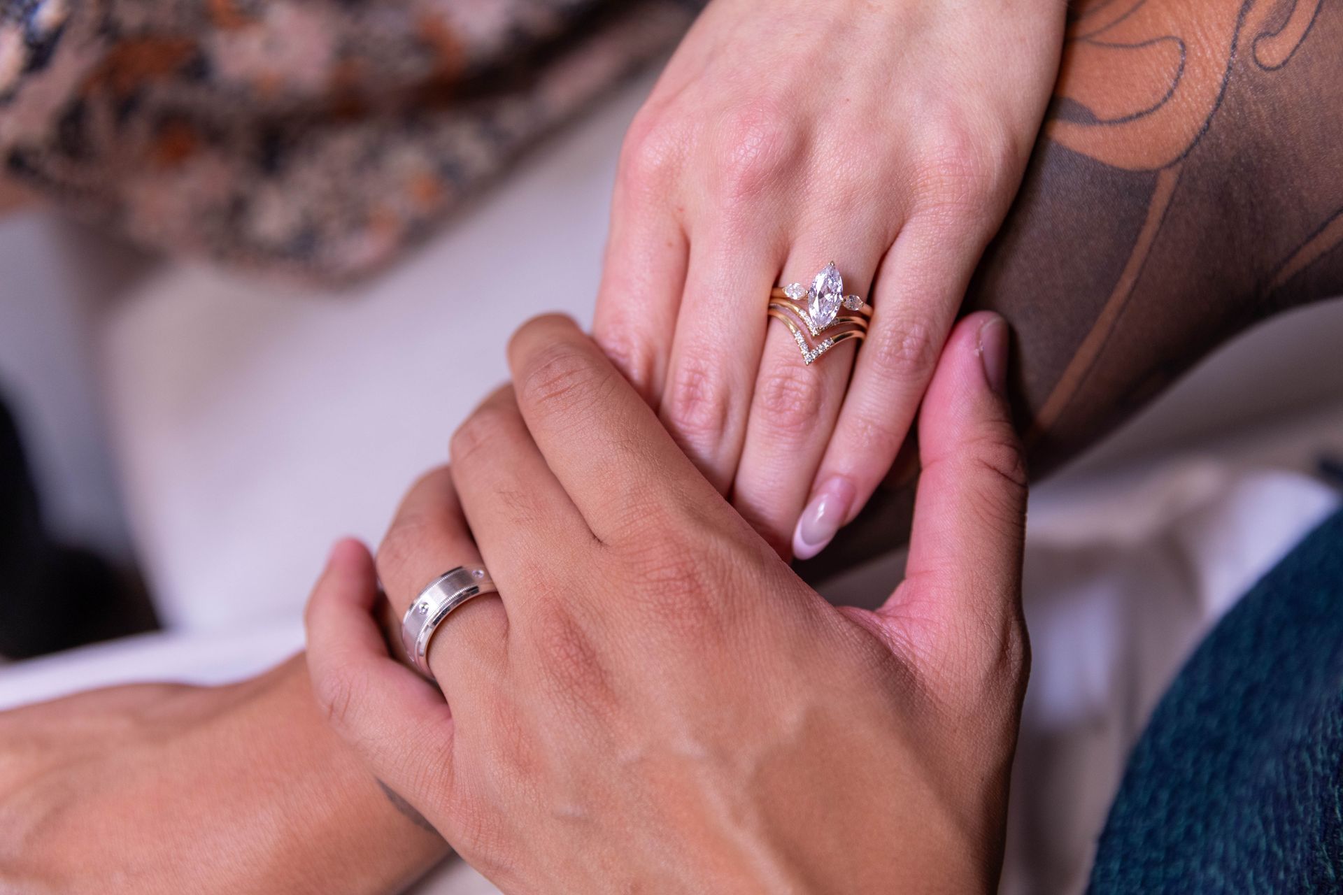 Two hands with wedding rings clasped together on a soft pink background.