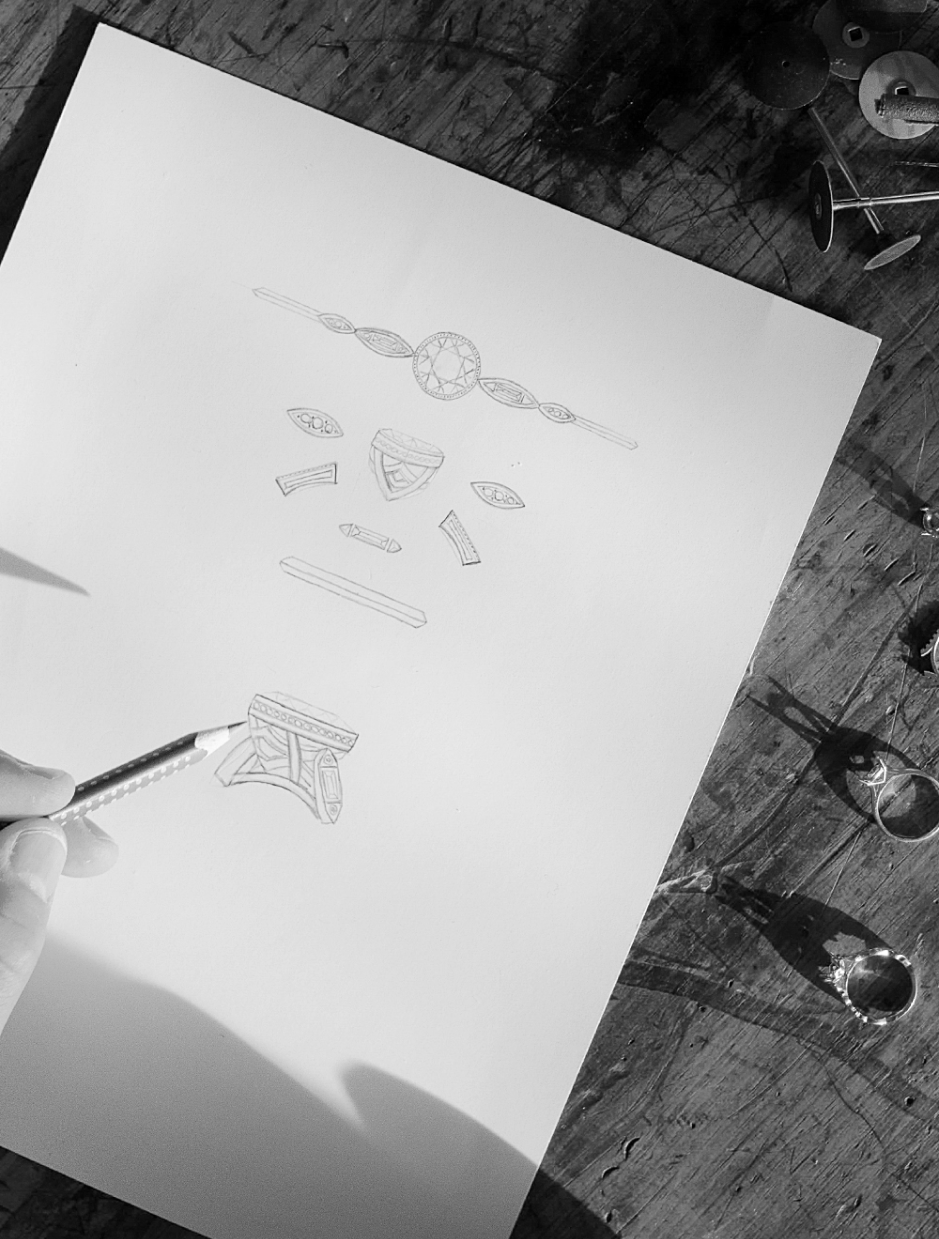 Hand sketch on white paper with a hand holding a pencil over a wooden table, with small objects nearby.