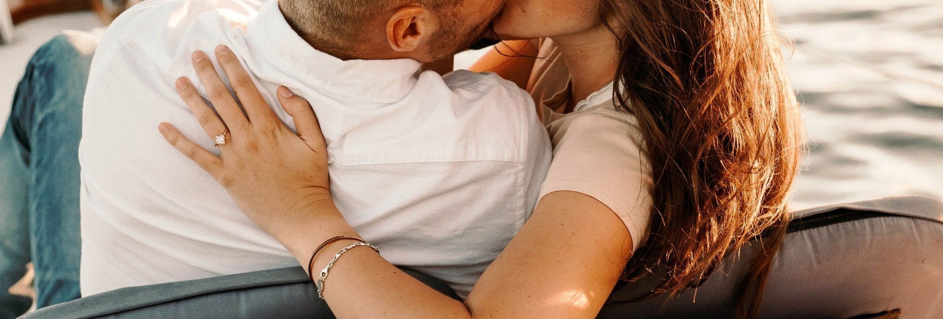 Two people embracing on a couch, with warm sunlight and a close-up view of their arms and faces.