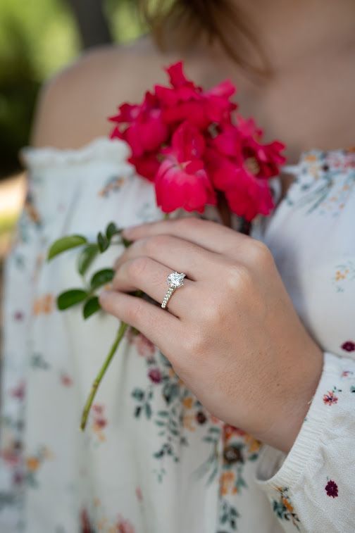 Hand holding bright pink flowers, wearing a floral dress and diamond ring