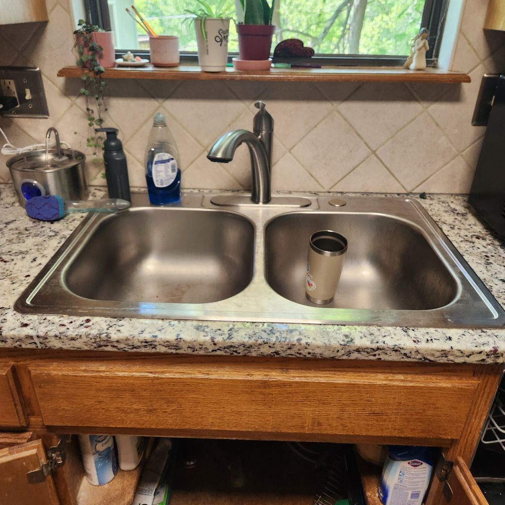Bright kitchen sink with gray countertop, white cabinets, and large windows overlooking greenery.