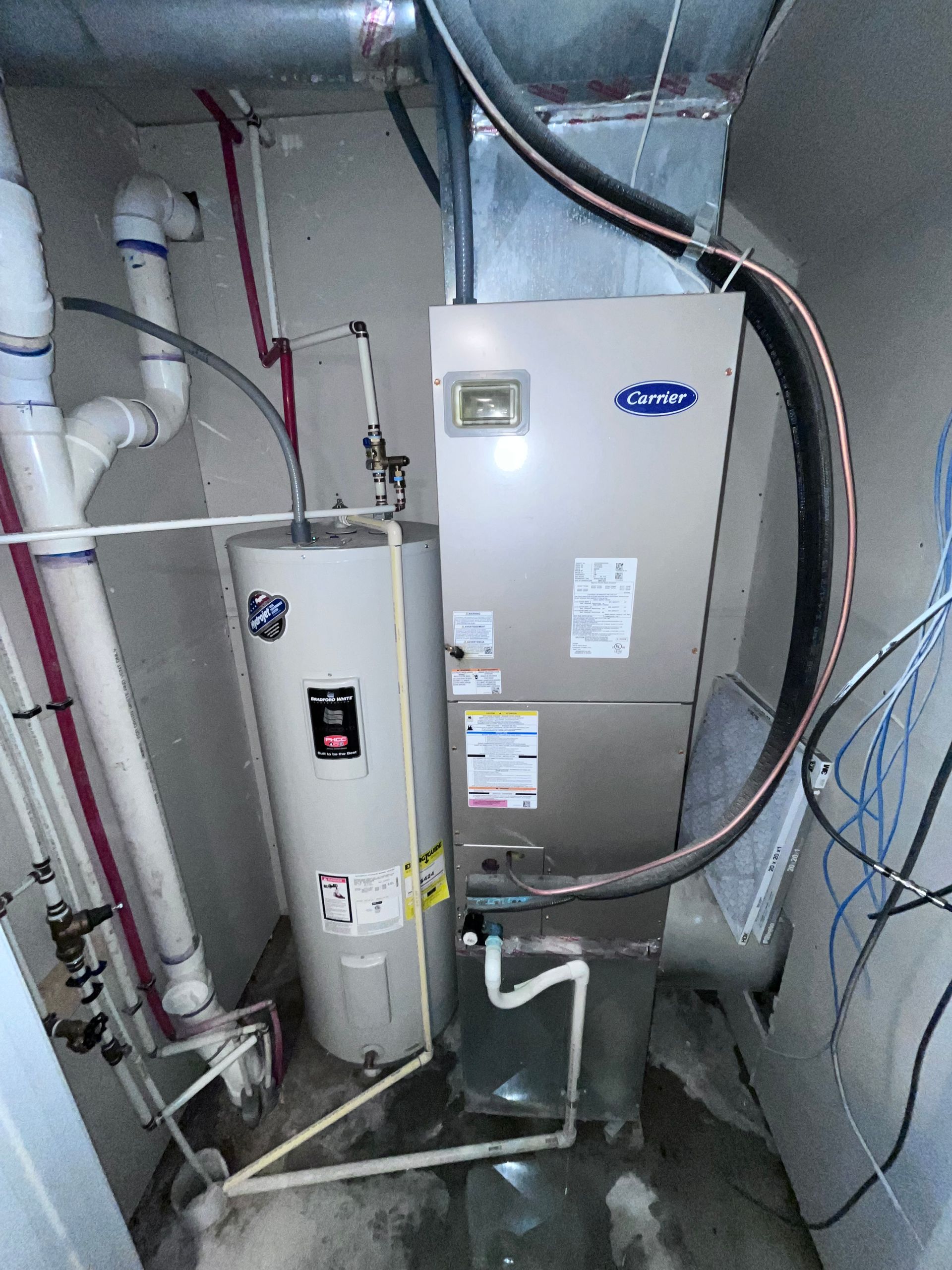 Narrow utility room with washer, water heater, shelves, cleaning supplies, and a small red rug.