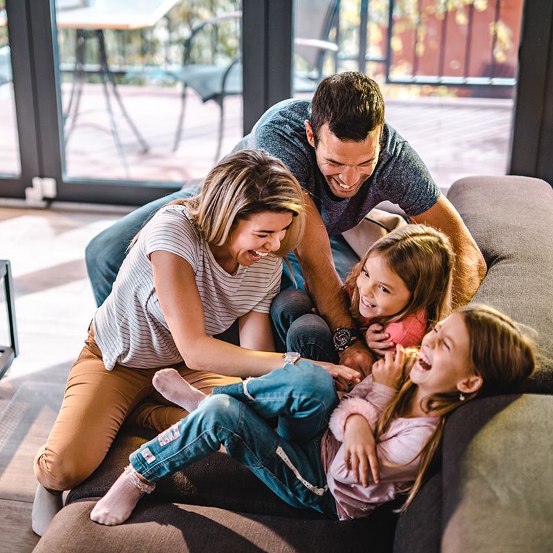 Family laughing and playing together on a couch in a bright living room