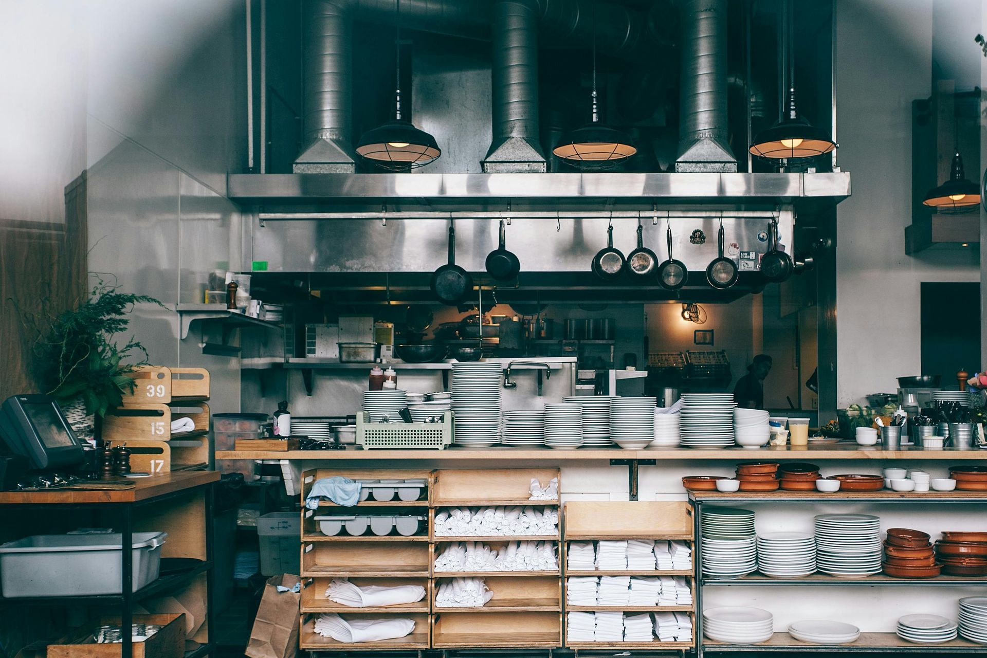 Cozy café kitchen with shelves of plates, bowls, jars, and hanging copper pans under warm lights