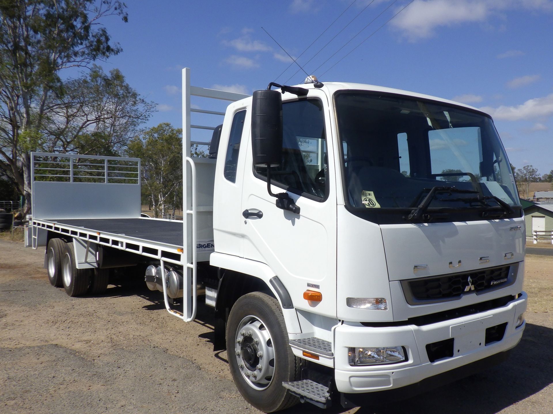 A white flatbed truck is parked on a dirt road.