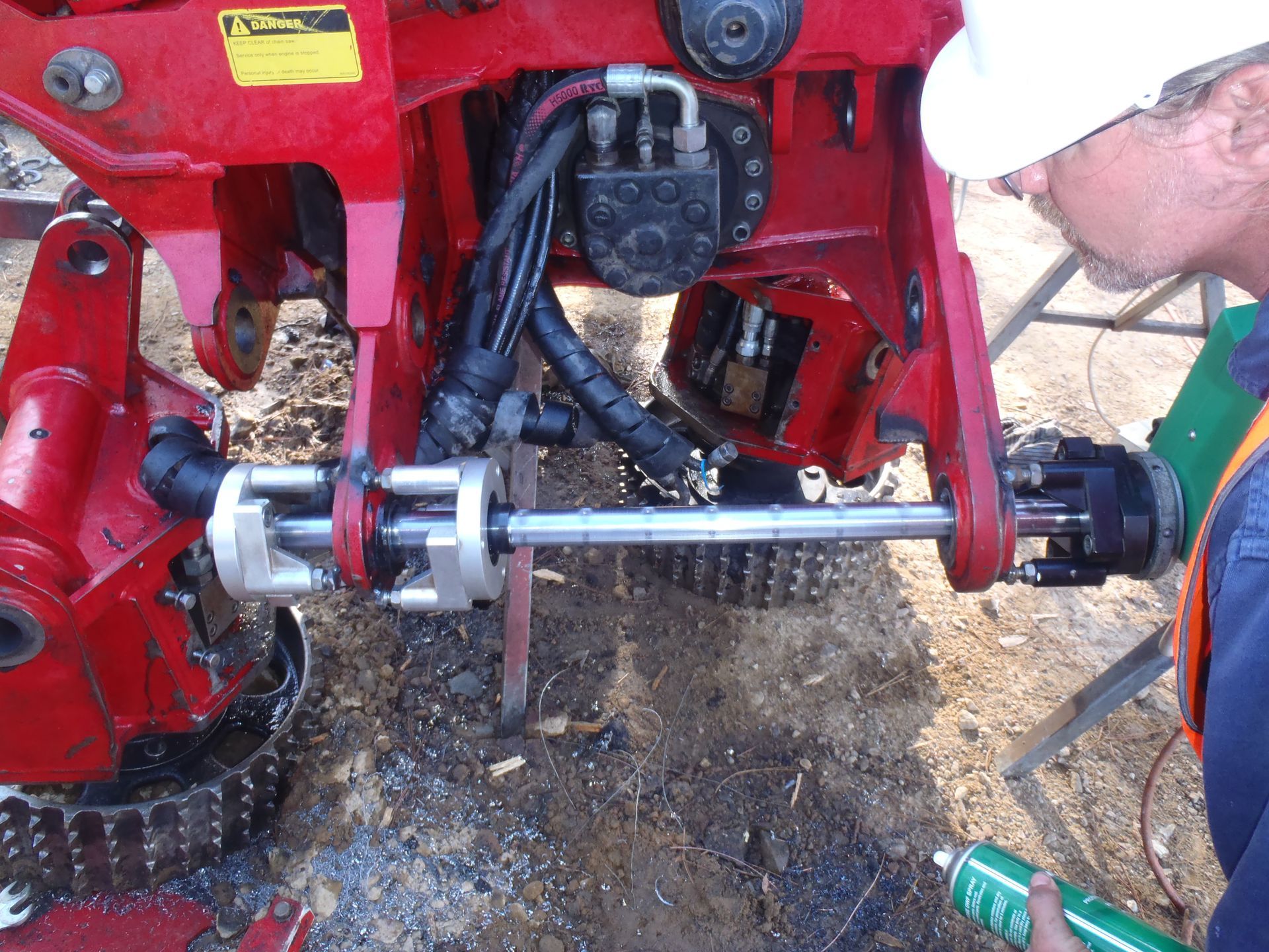 A man in a hard hat is working on a red tractor