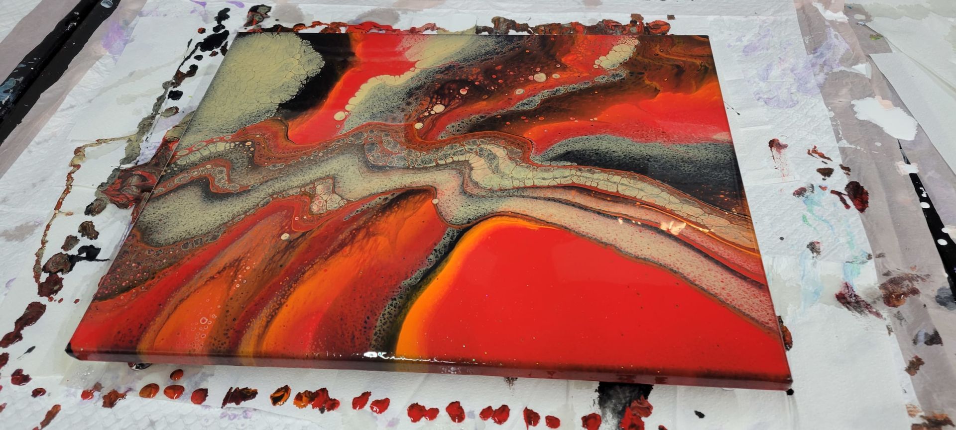 Abstract red, black, and gray fluid art painting on a table with paint splatters around it
