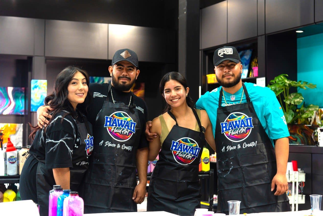 Four people in black aprons stand behind a colorful drink-making counter in a modern kitchen.