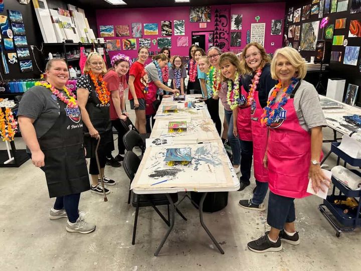 Group of people in colorful leis gathered around a long table in a craft shop