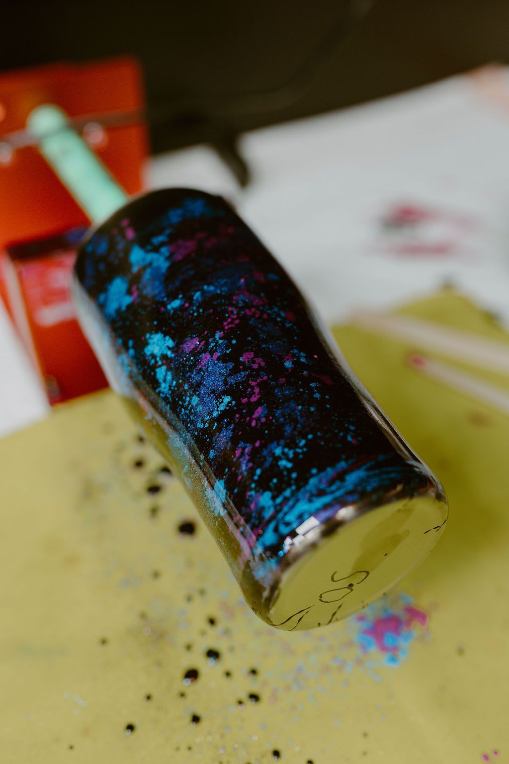 Glittery black cylinder lying on a yellow surface with scattered sparkles