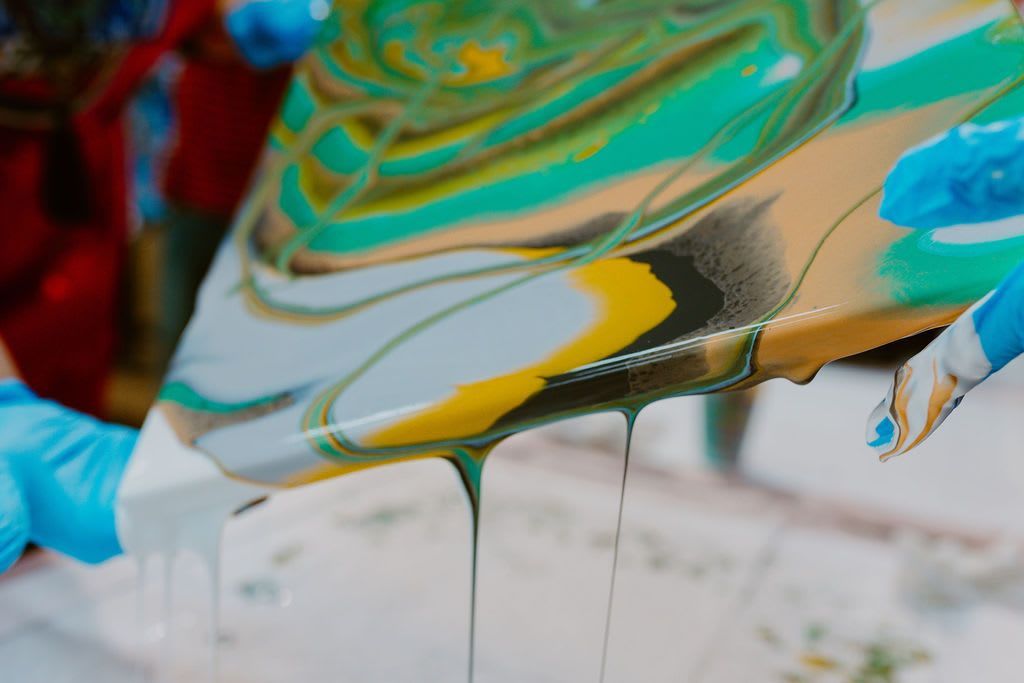 Pouring colorful paint onto a canvas, creating a swirling abstract pattern