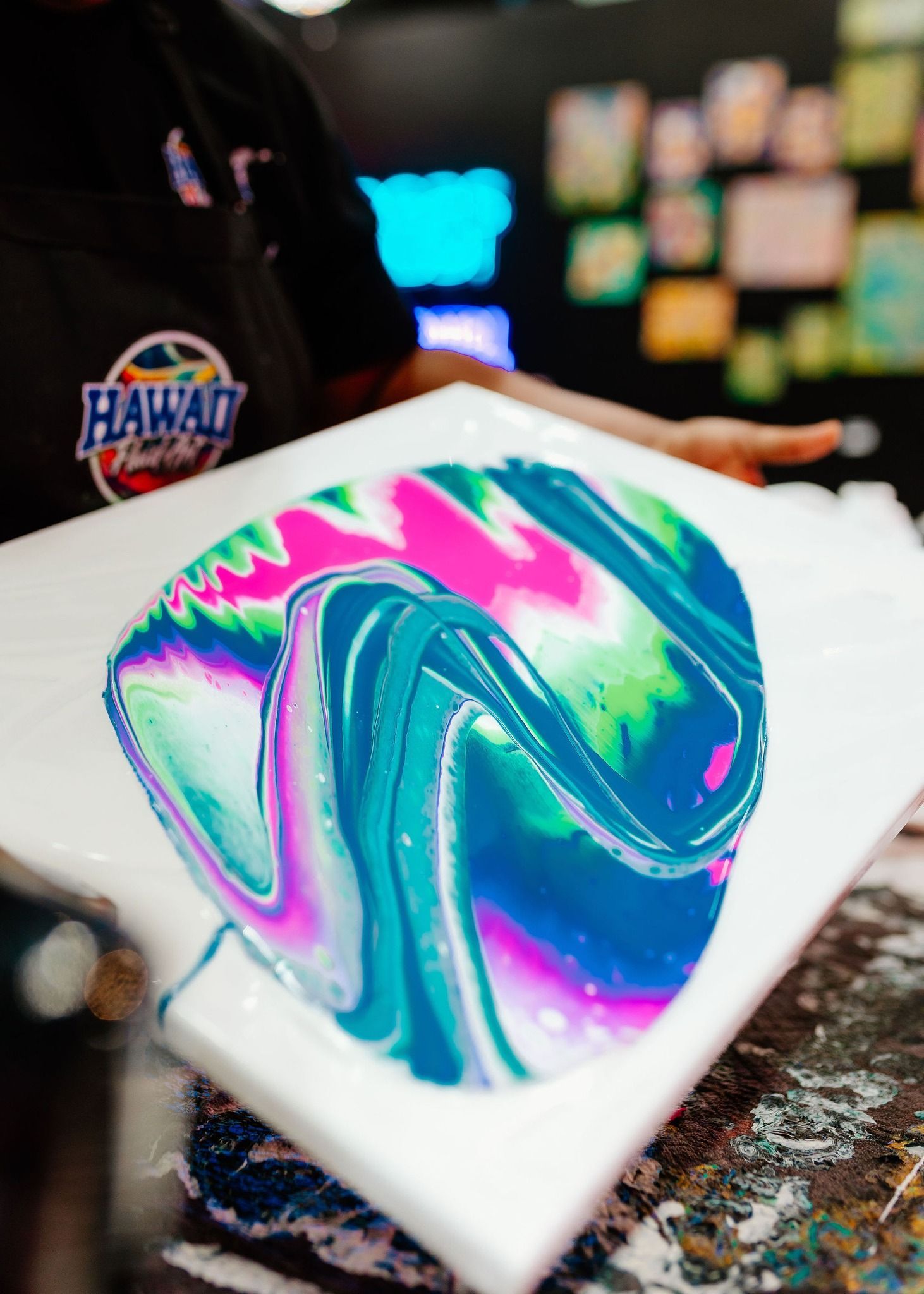 Swirled neon paint in turquoise, pink, and purple on a white canvas in a workshop