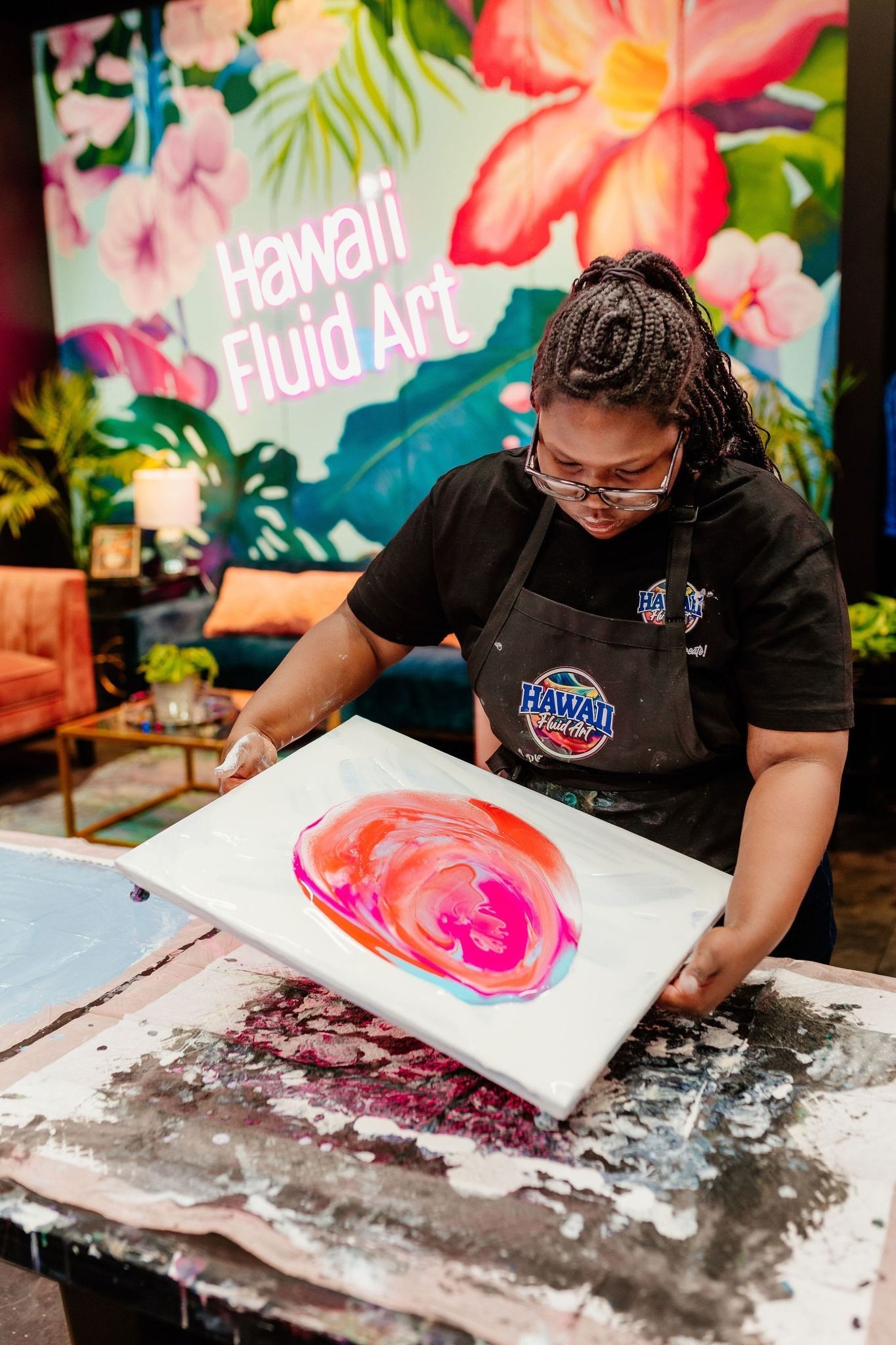 Artist painting a pink floral swirl on canvas at a colorful art festival booth